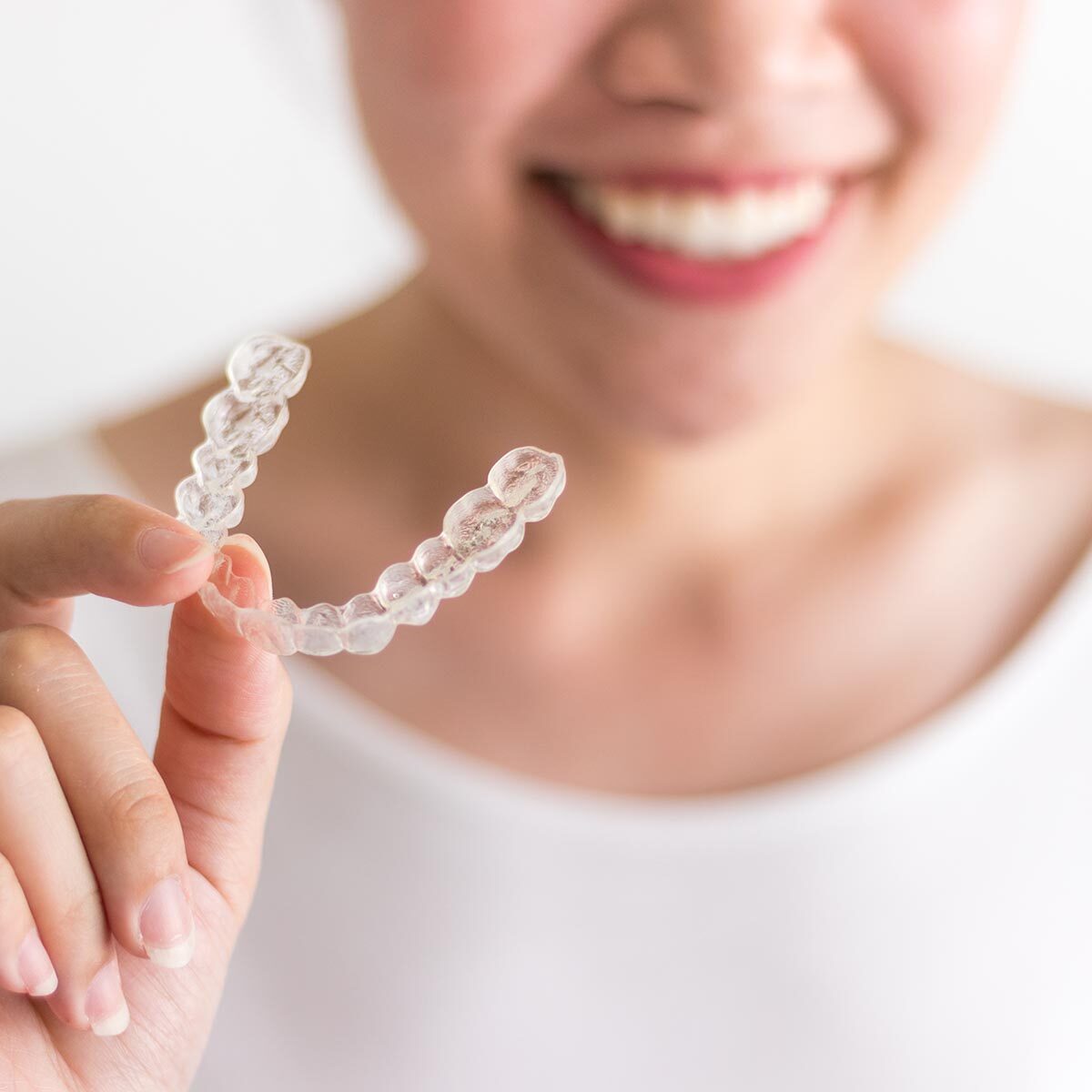 A smiling woman holding invisalign or invisible braces, orthodontic equipment