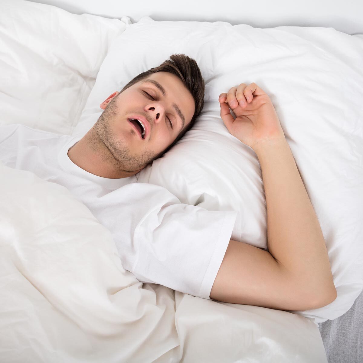 View Of Tired Young Man Snoring While Deep Sleeping In Bed