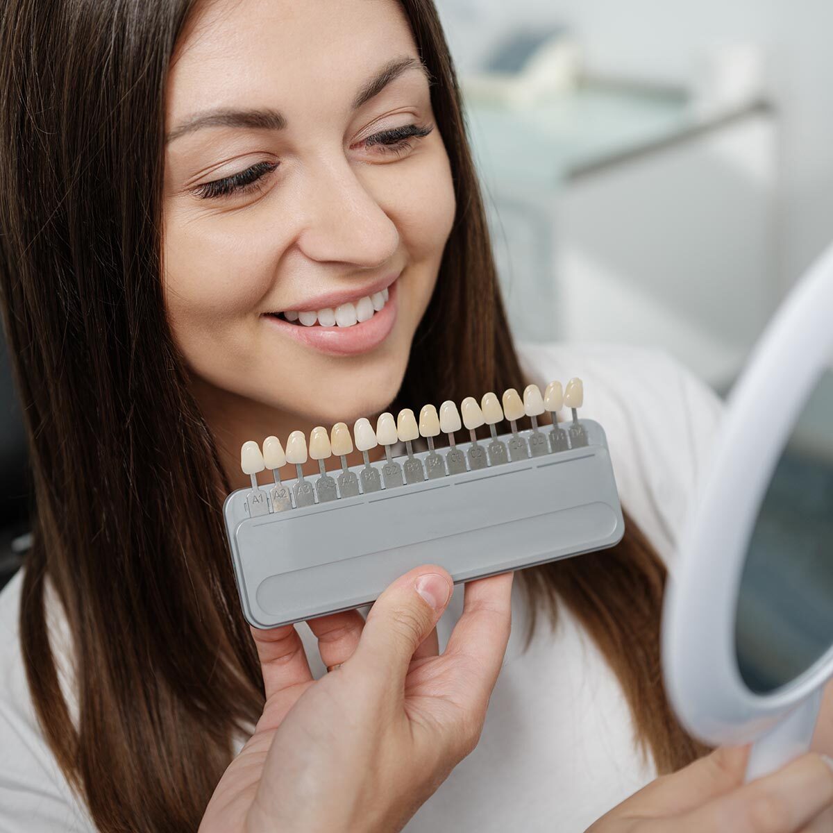 Young male dentist in white coat show veneers enamel color palette for beautiful patient woman sitting in a dental unit. Healthcare oral aesthetic treatment.